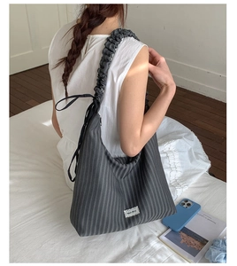Detail of grey pleated tote bag featuring ruffled strap and black ribbon bow accent