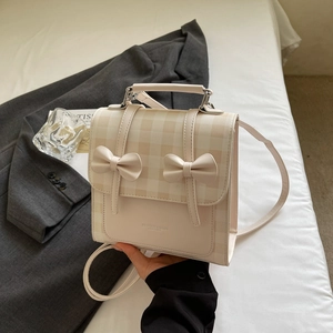 Detail shot of a cream PU leather backpack featuring yellow plaid and double bow accents