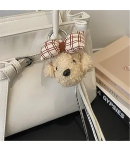 Close-up of cute plush dog charm with plaid bow hanging on white leather tote bag