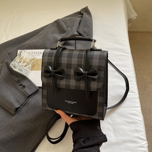 Detail of elegant checkered bow backpack placed on white bedding with minimalist decor