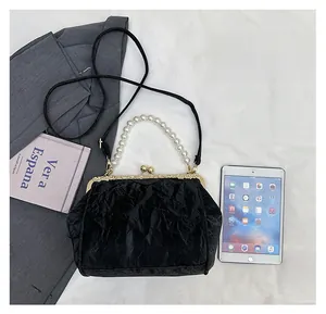 Detail of black pleated shell bag with pearl handle showing capacity next to an iPad