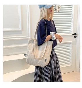 Detail of a large beige nylon tote bag with side woven label and soft pleated texture