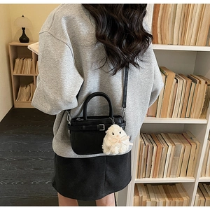 Detailed view of a black leather crossbody bag with a white plush bunny charm accessory