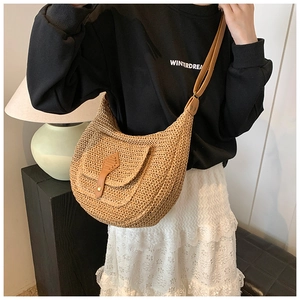 Detailed close-up of a woven straw half-moon bag featuring a brown leather buckle and strap