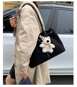 Close-up of black suede tote bag with cute plush bear charm on khaki trench coat