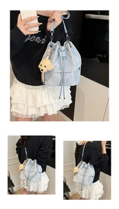 Detail of light blue bucket bag with pleated texture, drawstring, and bear charm