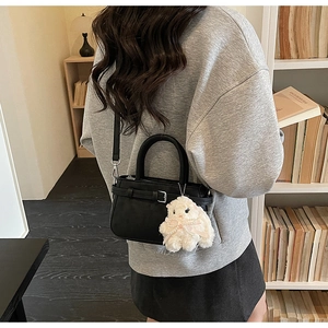 Close-up of black leather crossbody bag with buckle detail and white sheep pendant decor