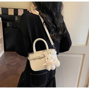 Side view of a white structured handbag with a cute plush charm worn by a model