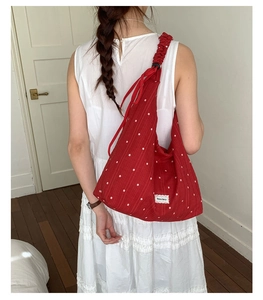 Detail of red floral tote bag showing ruffled shoulder strap and lace-edged logo label