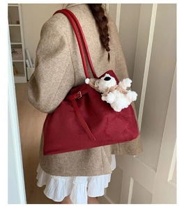 Detail of red suede boston bag with a cute teddy bear charm on a tweed jacket