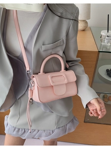 Detail of pink leather crossbody bag with flap square buckle shown on a grey suit outfit