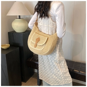 Detail of a large straw shoulder bag worn by a model in a minimalist interior setting