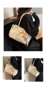 Detail view of cream-white tote bag with teddy bear charm and tassel on black outfit