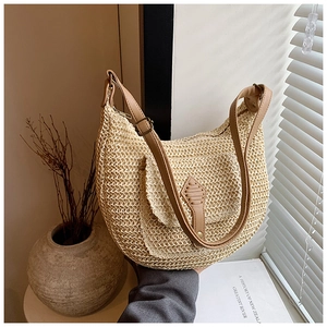 Close-up of crescent straw bag featuring a brown leather strap and front pocket detail