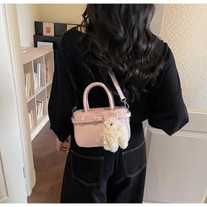 Detail of cherry pink small square bag with decorative buckle and plush rabbit charm