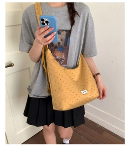 Macro detail of yellow polka dot canvas crossbody bag showing texture and logo label