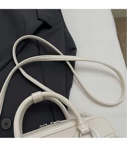 Detailed view of the beige leather handbag featuring a slender shoulder strap and silver buckles