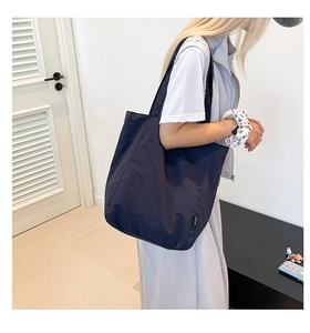 Detail of navy blue large capacity tote bag with wide shoulder strap on model in minimalist room