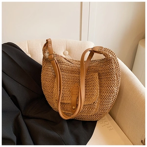 Detailed close-up of handmade straw hobo bag with brown faux leather strap on soft sofa