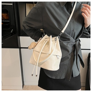 Detailed view of a creamy white drawstring bucket bag with side zipper and crossbody strap