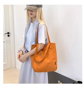 Detail of an orange canvas tote bag with long shoulder straps and black woven side label