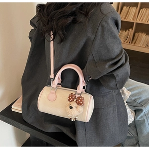 Pink cylinder handbag with plush bear charm on grey suit model background