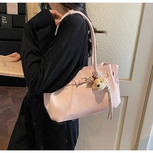 Detail of pink patent leather tote bag featuring a decorative belt and cute plush bear charm