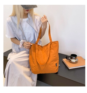 Detail view of a large orange nylon tote bag with shoulder straps held by a model