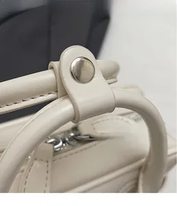 Close-up of cream white leather handbag featuring a silver metal snap and zipper detail