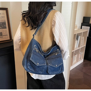 Detail of blue denim hobo bag featuring multiple pockets and silver metallic zippers