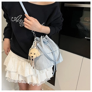 Detail of light blue drawstring bucket bag with plush puppy charm and printed ribbon strap