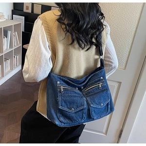 Detail of blue denim crossbody bag with cargo pockets and metallic buckles worn by a model