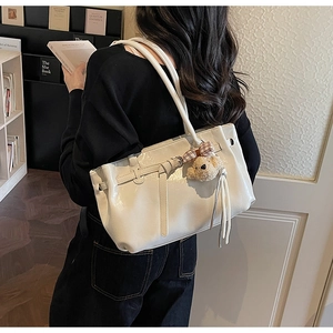 Detail of white glossy leather tote bag with plush bear charm and elegant long tassels