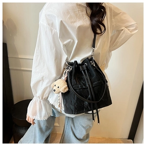 Detail of black drawstring bucket bag with beige plush puppy charm on a model