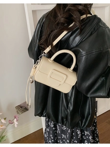 Detail shot of a beige square handbag with decorative buckle worn by a model in a leather jacket