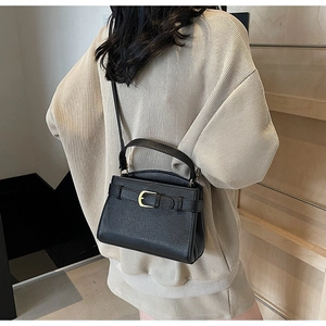 Détail d'un sac à main noir en cuir grainé avec boucle en métal doré et bandoulière