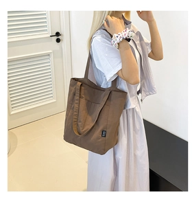 Detail of a brown nylon tote bag with a black brand label shown in a modern interior