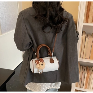 Detail of white leather boston bag with brown handles and a cute plush bear charm