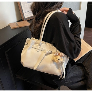 Detail of off-white tote bag featuring decorative belt and plush bear charm pendant