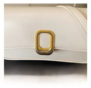 Close-up of golden rectangular metal lock with vertical texture on cream leather bag