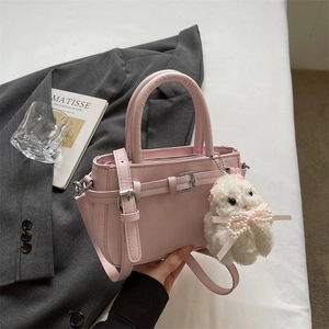 Close-up of pink leather handbag featuring a plush bunny charm and metallic buckle