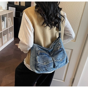 Detail of blue denim shoulder bag with multiple pockets worn by a model in casual setting