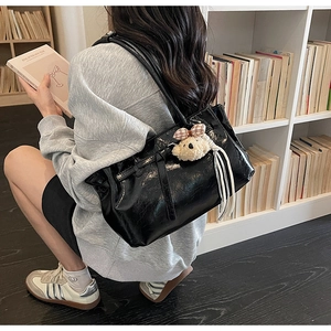 Glossy black tote bag detail featuring a plush bear charm in a cozy library setting