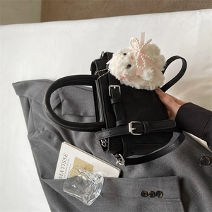Close-up of black leather handbag featuring adjustable buckle straps and a plush charm