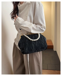 Detail of black pleated shell bag with large pearl handle and vintage gold metal clasp