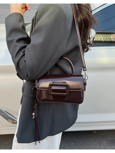 Detail of dark brown glossy leather crossbody bag with square buckle and tassel accent