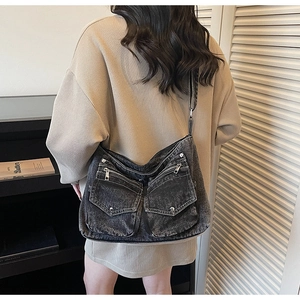 Detail view of washed black denim crossbody bag with dual pockets and metal accents