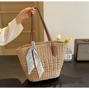 Detail of hand-woven straw tote with brown faux leather handles and floral scarf