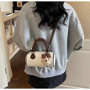 Detail showing white boston pillow bag with brown straps and cute teddy bear charm