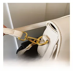 Close-up of golden metal hooks and precise stitching on a white leather shoulder bag